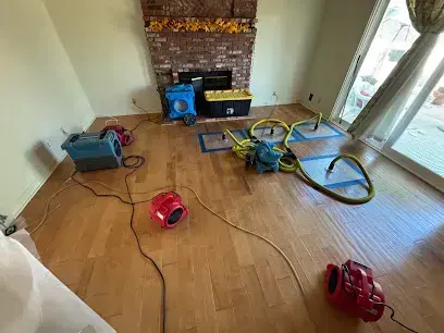 Air movers and a dehumidifier drying a living room with wood floors in Menifee