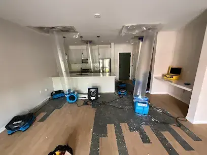 Air movers and plastic containment drying a living room with plank flooring partly removed