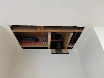 Ceiling drywall cut open below attic pipes and ductwork after an AC condensate leak