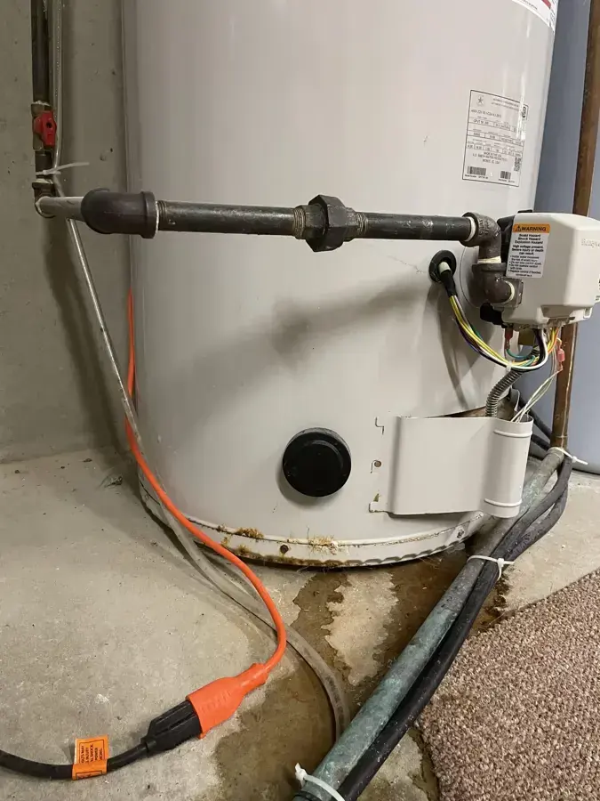 Tank water heater with leaked water spreading across the floor at its base